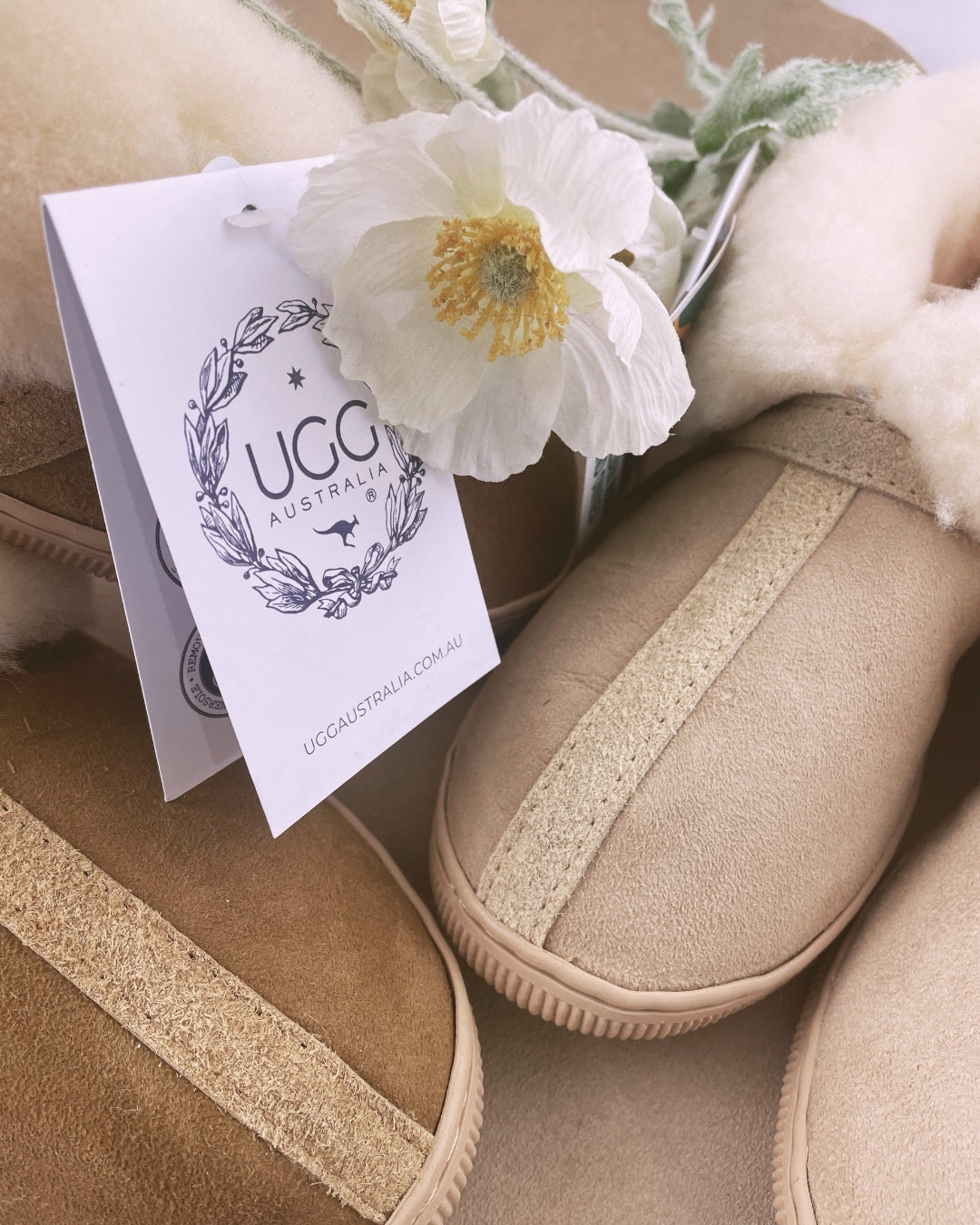 Beige slippers with a UGG Australia tag and white flowers in the background